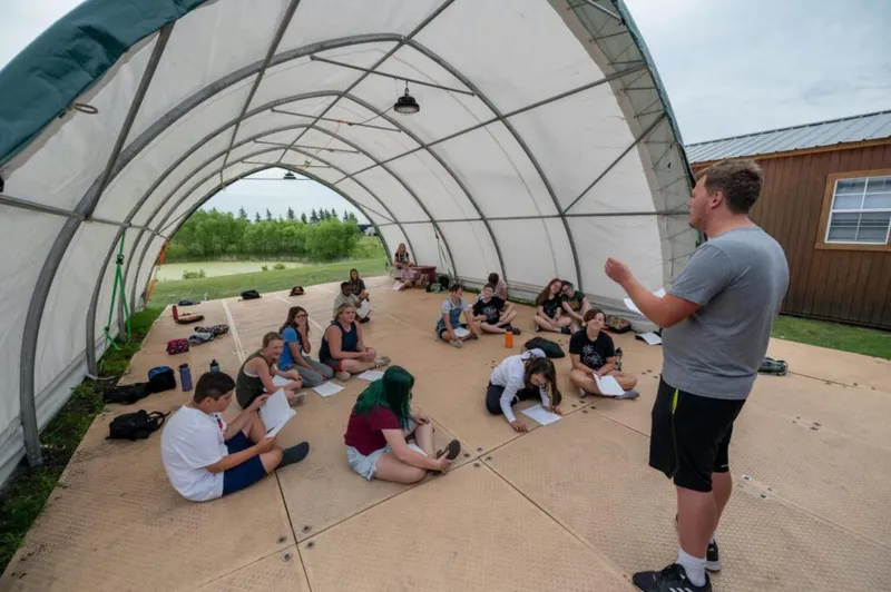 Instructor addresses a group of teens seated on the floor inside a large open-ended tent structure