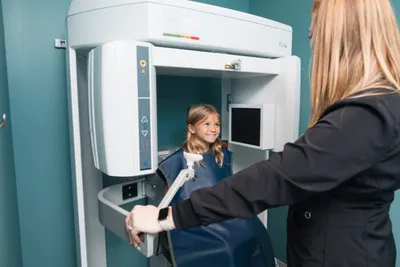Young girl in dental X-ray machine as a clinician in gloves positions the equipment