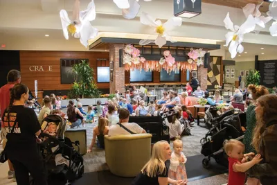 Crowded indoor museum lobby filled with families and young children beneath large paper flower installations
