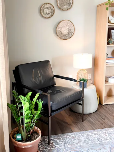 Black leather armchair in a styled corner with woven wall decor, table lamp, and potted plant