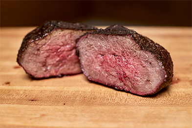 Sliced medium-rare beef roast with dark crust resting on a wooden cutting board