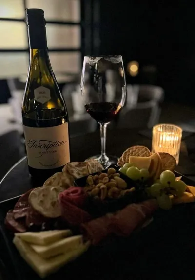 Charcuterie board with cheese, grapes, and crackers beside a red wine glass and candle