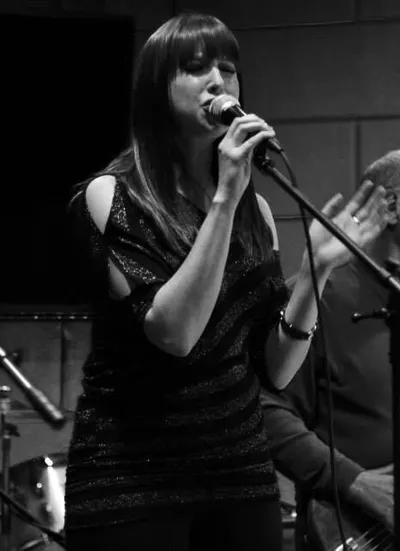 Woman with dark hair singing into a microphone in black and white
