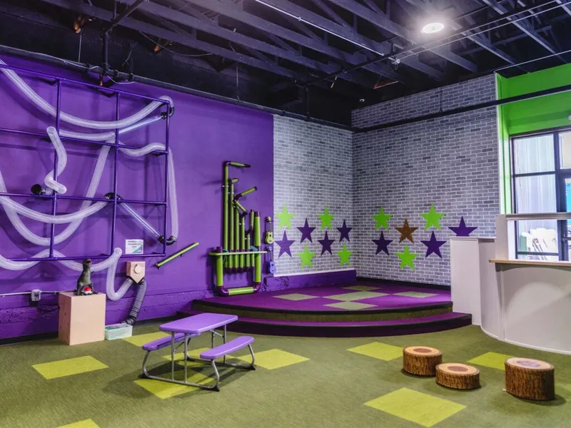 Colorful children's museum play room with purple walls, star decals, tube wall, and small stage