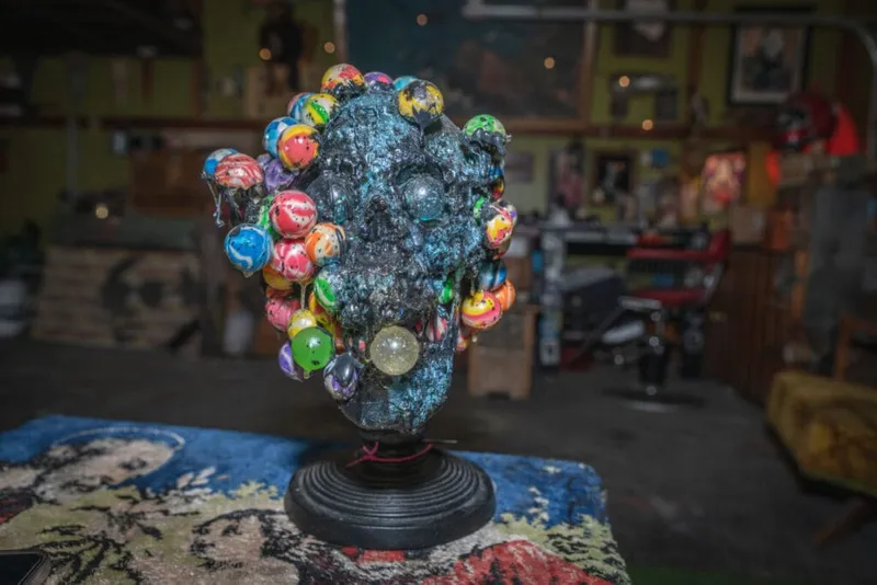 Dark sculptural head covered in colorful bouncy balls on a black pedestal