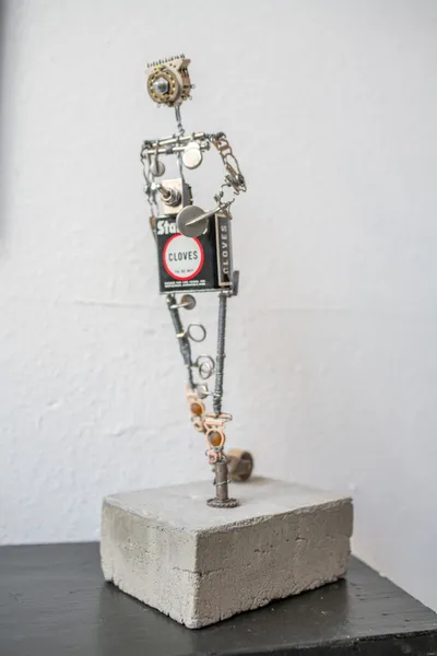 Humanoid figure sculpture made from salvaged metal parts and a cloves tin, mounted on a concrete block