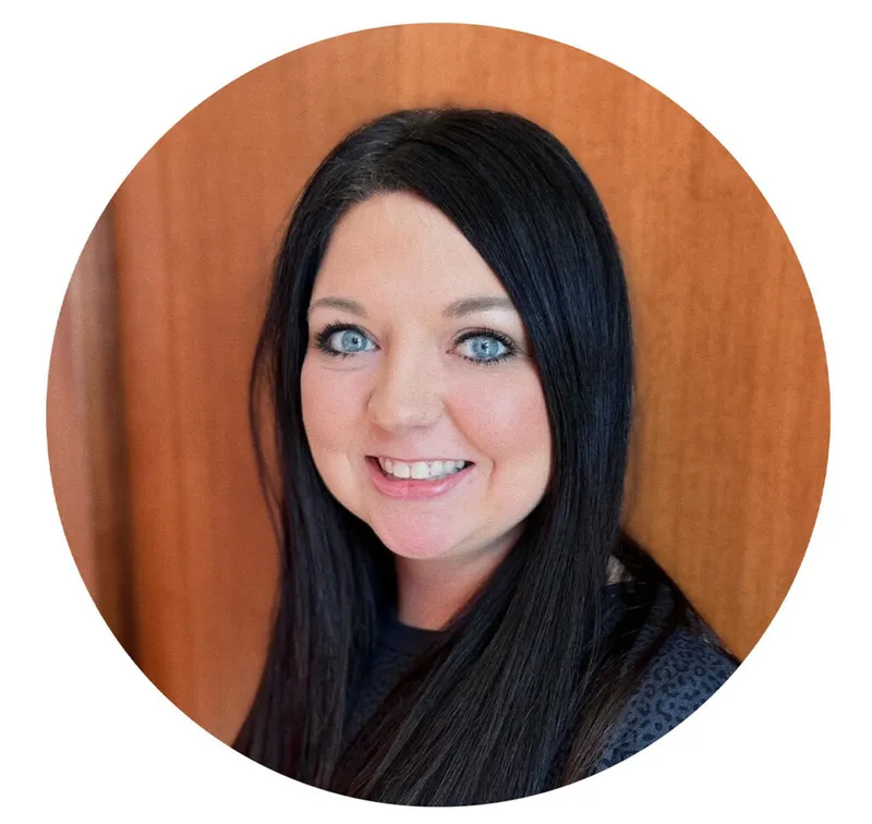 Smiling woman with long black hair and blue eyes against a wood-paneled background