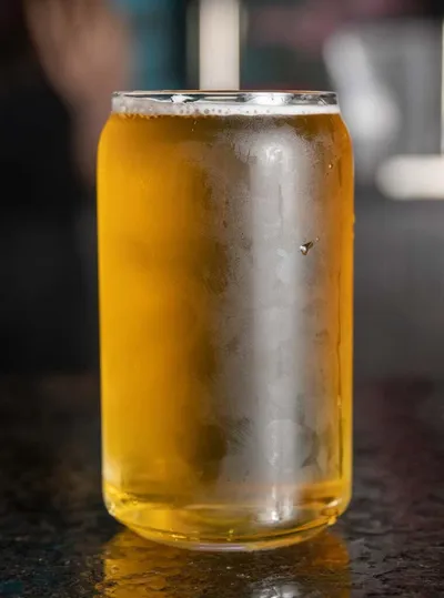 Condensation-covered can-shaped glass filled with golden beer on a dark bar top