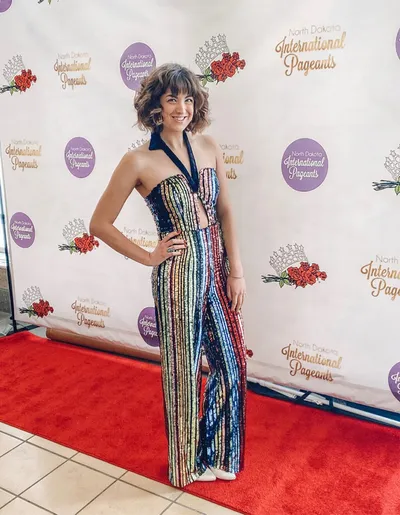 Woman in a multicolor sequined halter jumpsuit posing on a red carpet in front of a North Dakota International Pageants