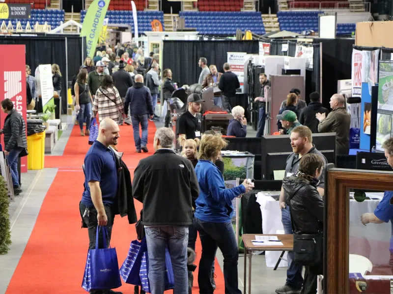 Crowd of attendees walking among vendor booths on a red-carpeted arena floor at an indoor home and garden show