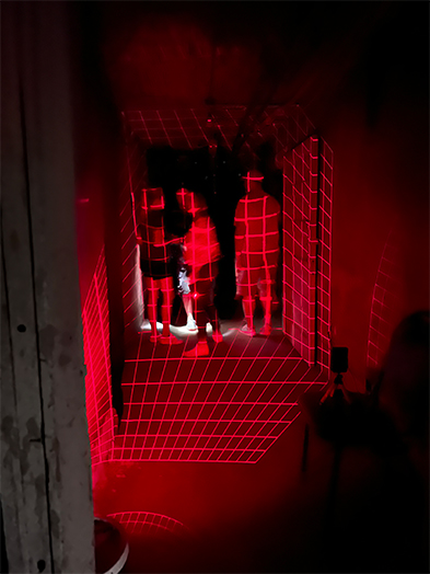 Silhouettes of people in a dark corridor bathed in eerie red light with grid projections