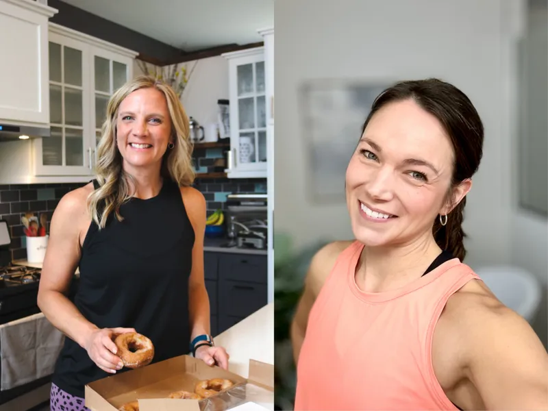 Two smiling women in athletic wear, one holding a donut in a kitchen, one taking a selfie