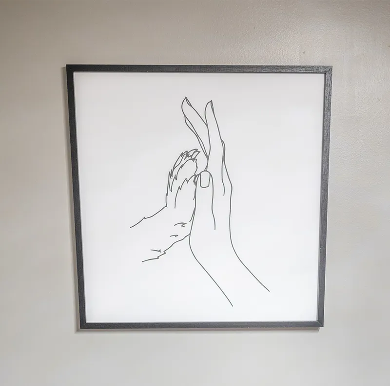Framed minimalist line drawing of two hands touching, in a dark wood frame on a grey wall
