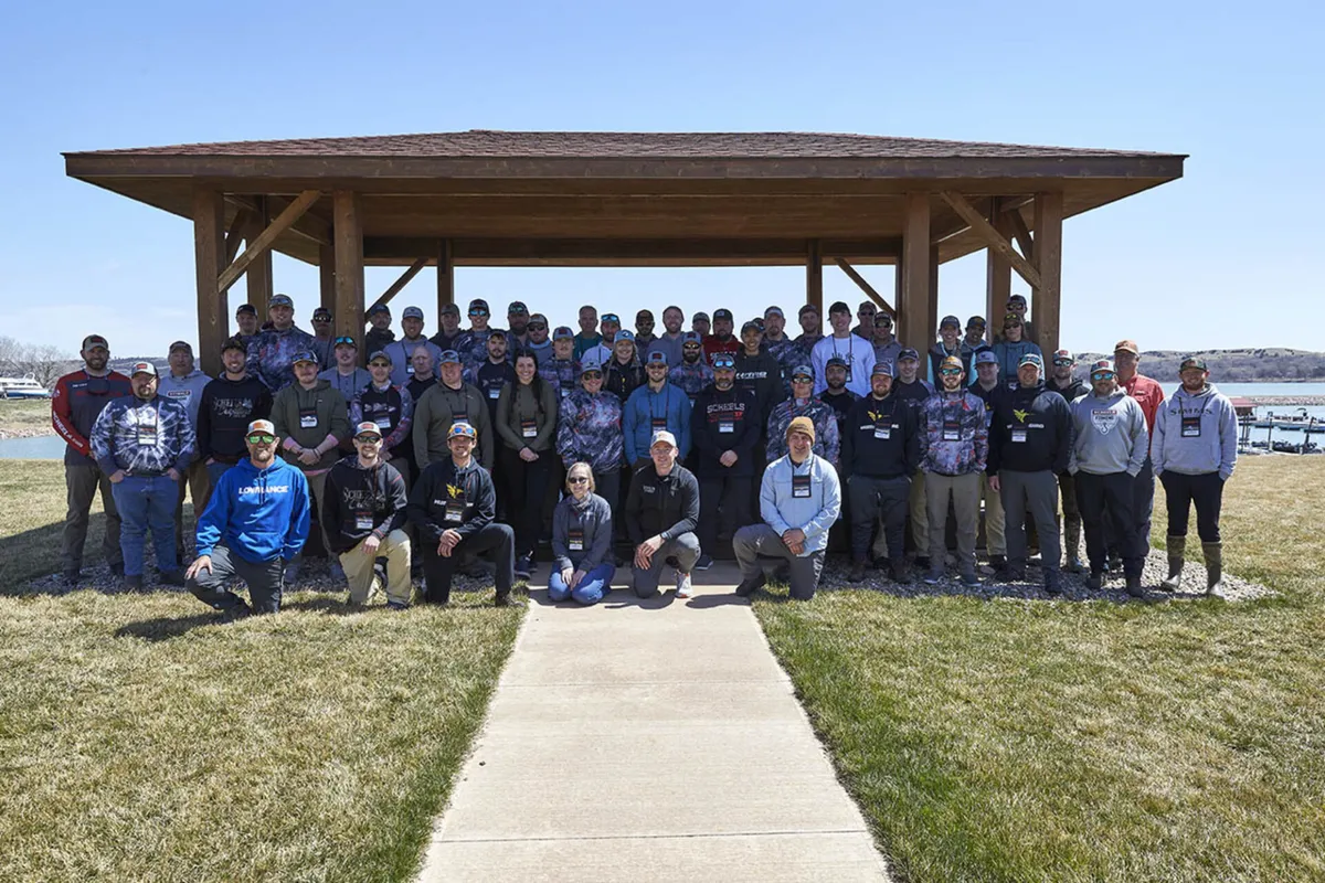 Large group of people posing under a wood pavilion near a lake on a sunny day