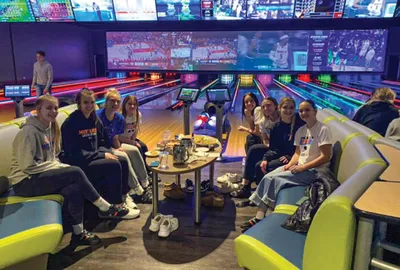 Group of teens seated around a table in a colorful bowling alley lounge area