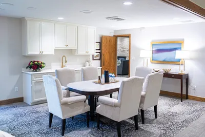 Bright reception room with round dining table, cream upholstered chairs, white cabinetry, and colorful abstract wall art