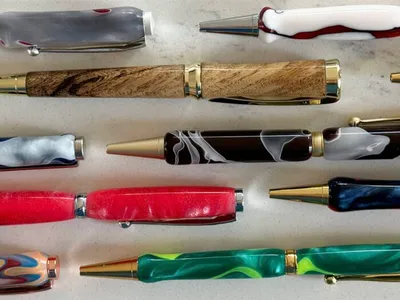 Assorted handcrafted pens with colorful resin and wood barrels arranged on a white surface