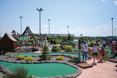 Families playing mini golf on a landscaped outdoor course with a large slide in the background