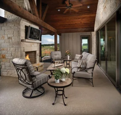 Covered stone patio with wrought-iron seating, lit fireplace, wood-beam ceiling, and sliding glass doors