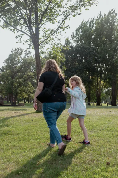 Woman and young girl walking together across a grassy park lawn
