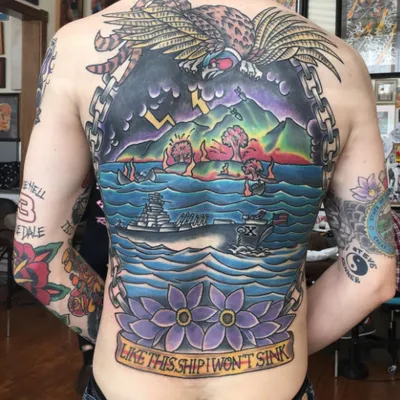 Person's fully tattooed back featuring an eagle, warship, mountains, and banner reading 'Like This Ship I Won't Sink