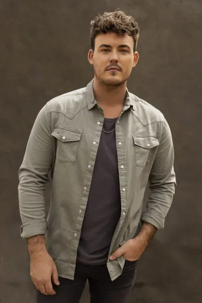 Young man in an open grey western shirt over a dark tee, hands in pockets