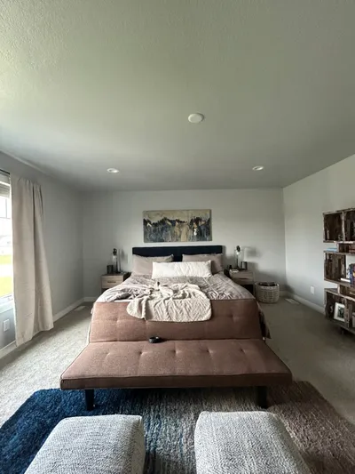 Neutral-toned bedroom with rust bench, layered rugs, and abstract art above bed