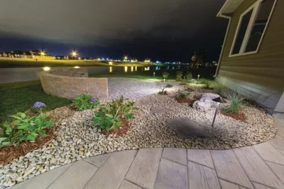 Nighttime landscaped yard with gravel garden bed, low plants, and path lighting near a home