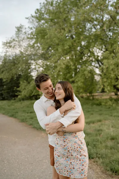 Couple embracing and smiling on a park path surrounded by green trees