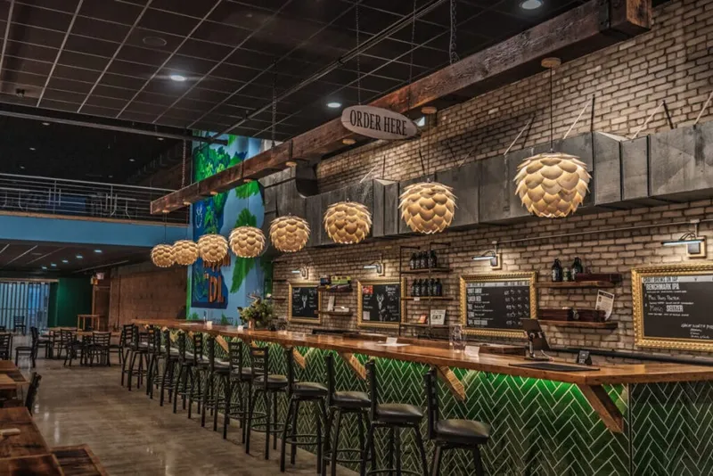 Long wooden bar with pineapple-style pendant lights and green herringbone tile beneath an "Order Here" sign