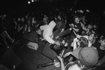 Crowded black-and-white concert scene with a performer leaning into the audience