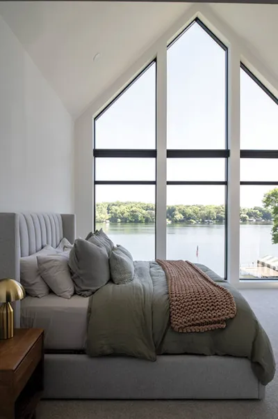 Modern bedroom with vaulted peak windows overlooking a tree-lined lake