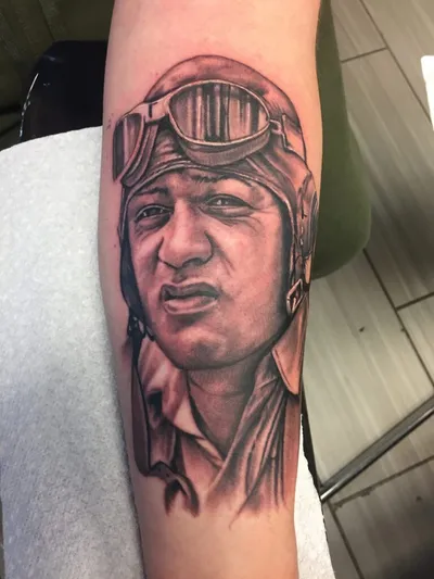 Black and grey portrait tattoo of a man in a pilot's helmet and goggles on a forearm