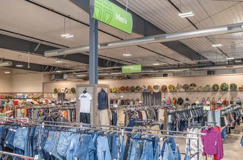 Thrift store interior with racks of jeans and clothing beneath Men's and Women's department signs