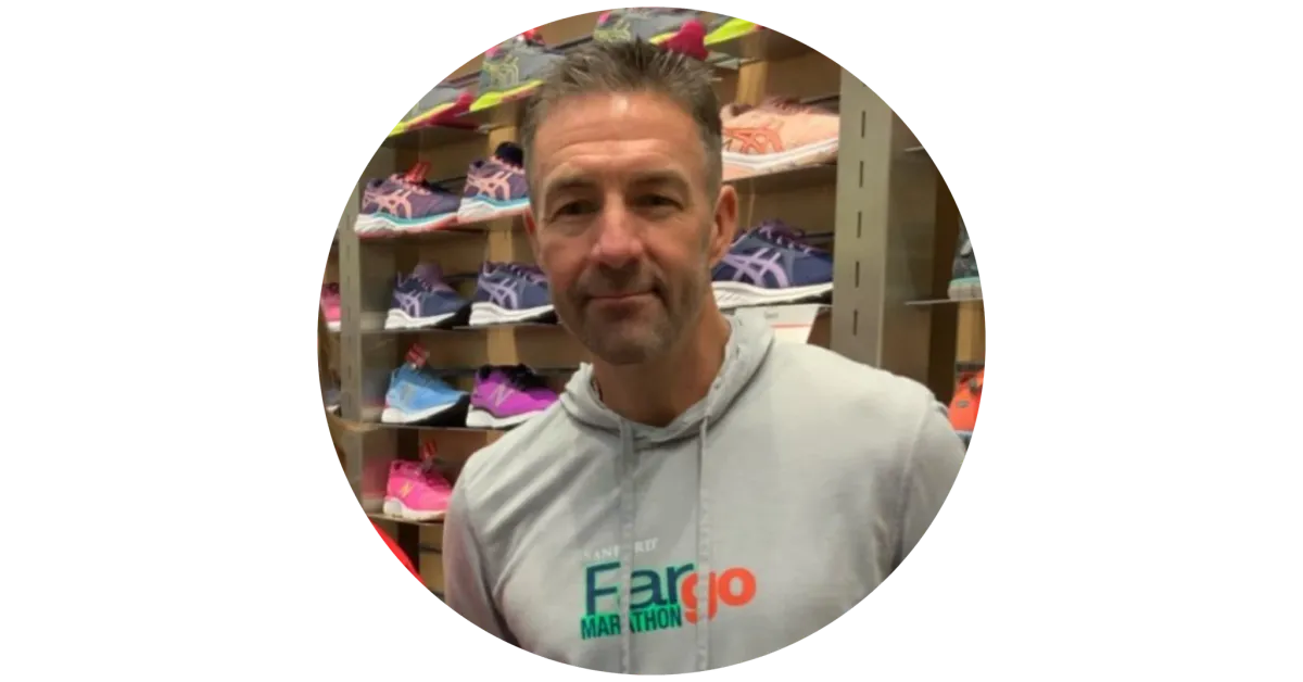 Man in a Fargo Marathon hoodie standing in front of shelves of colorful running shoes