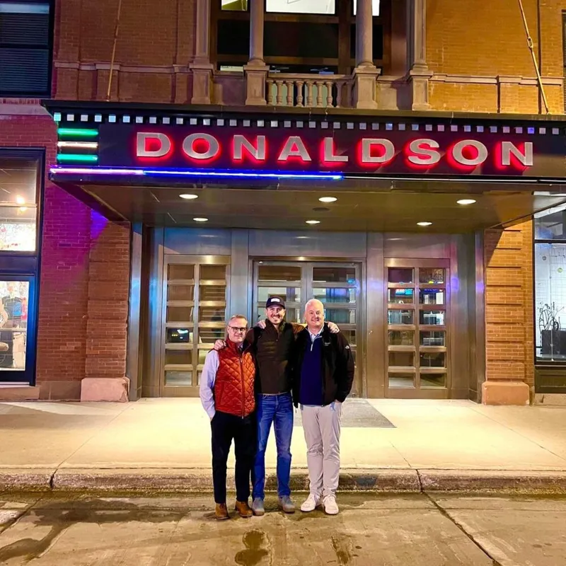 Three men standing together outside the lit Donaldson marquee at night