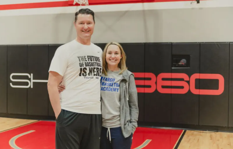 Tall man and woman smiling on a basketball court inside a Shoot 360 facility