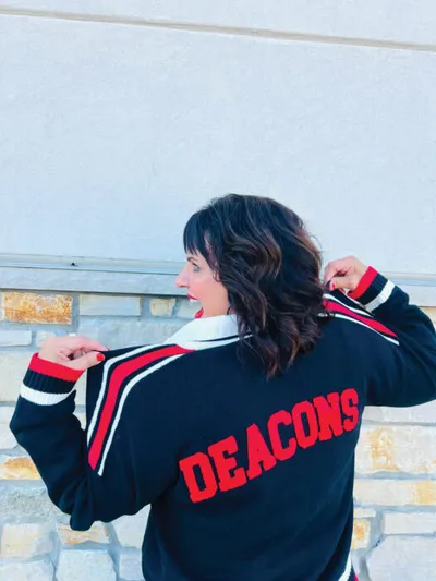 Woman showing back of black varsity jacket with red Deacons lettering