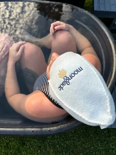 Person soaking in an outdoor metal tub holding a white Moonglade exfoliating mitt