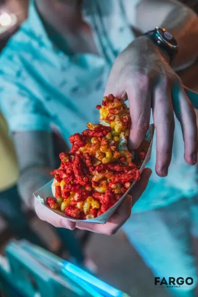 Hand holding a cardboard tray overflowing with red and yellow puffed corn snacks
