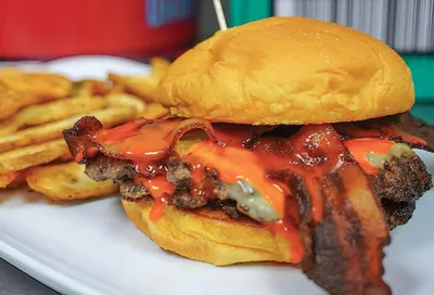 Bacon cheeseburger with orange sauce served alongside seasoned fries on a white plate