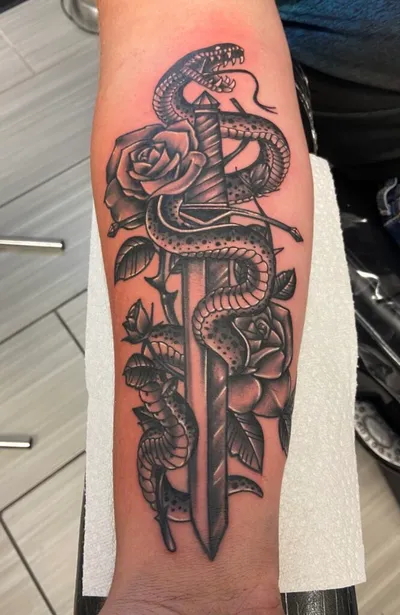 Black and grey forearm tattoo of a snake coiled around a dagger with roses