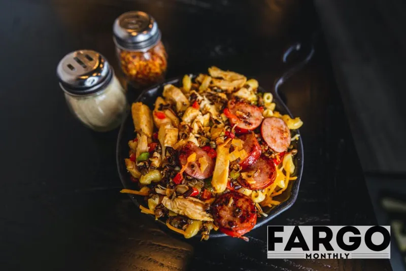 Cast iron skillet of mac and cheese topped with sliced sausage, peppers, and chicken