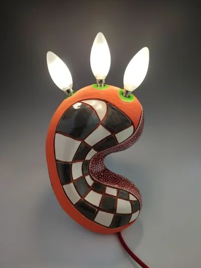 Ceramic kidney-shaped lamp with black-and-white checkerboard pattern and three lit candelabra bulbs