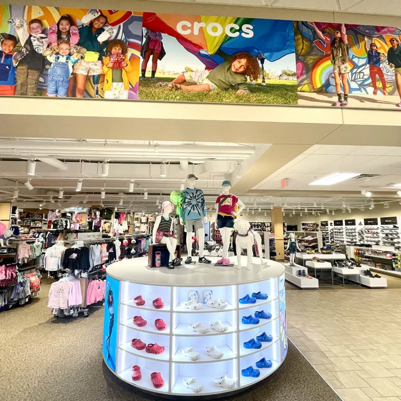 Crocs display kiosk with lit shelves of colorful clogs and child mannequins inside a large retail store