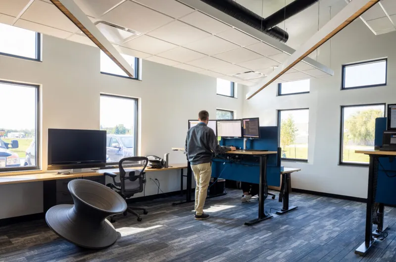 Man working at a standing desk in a modern open office with high ceilings and large windows