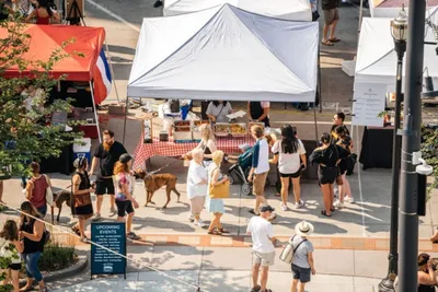 Aerial view of an outdoor market with white tents, vendors, and shoppers on a sunny day