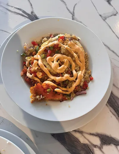Overhead view of a grain bowl with diced vegetables and drizzled orange sauce in a white bowl on marble