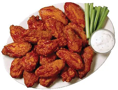 Plate of saucy buffalo chicken wings with celery sticks and ranch dip
