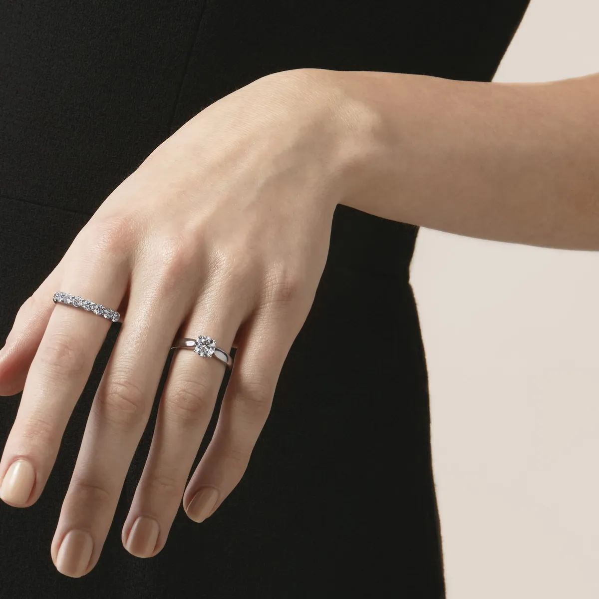 Woman's hand wearing a round solitaire engagement ring and a diamond eternity band in white metal